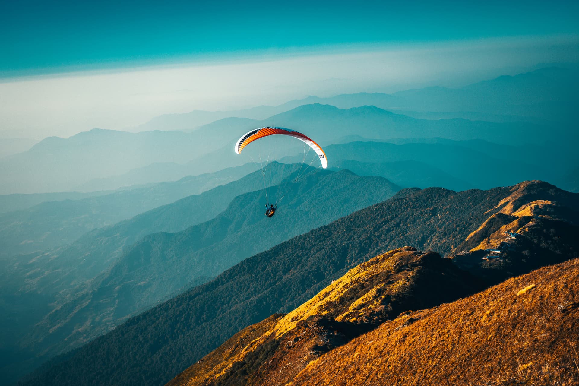 Paraglider met oranje scherm boven een bergketen in ochtendlicht